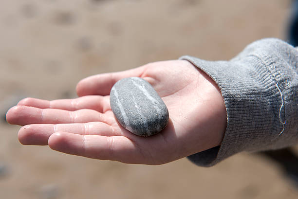 An outstretched hand, palm open, with a singular, slightly dirty pebble in the center.