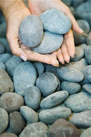 Two hands cradling three pebbles, with dozens of other pebbles surrounding the hands.
